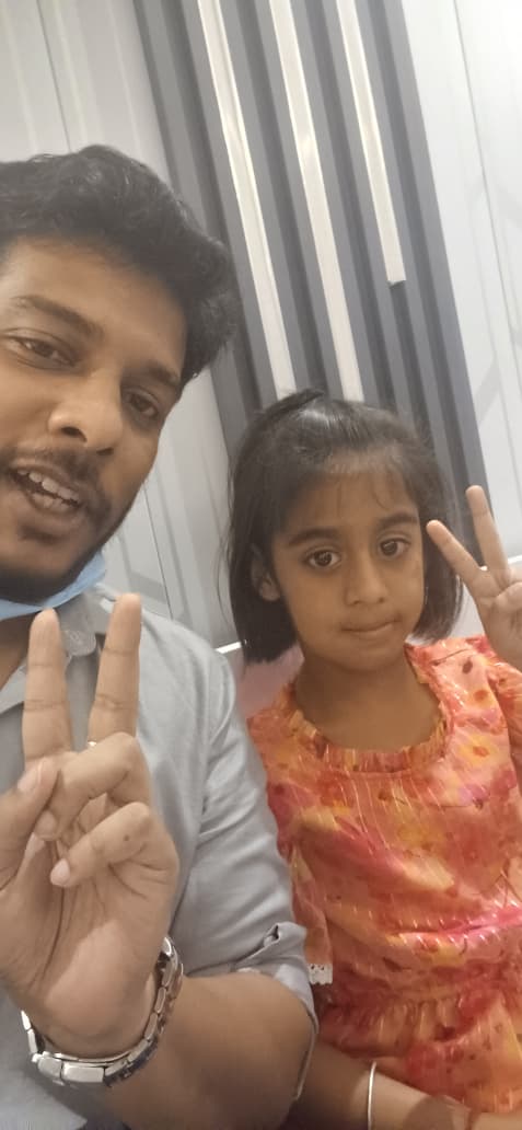 A young girl making a peace sign beside Dr. Rangan Ghosh after her dental check-up at Tiny Tooth Dental